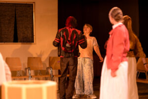 Vier Jugendliche in einem Innenraum spielen eine Szene, zwei im Vordergrund, zwei im Hintergrund.