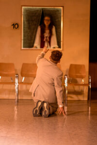 Mann kniet vor Stühlen und reicht Hand zu Frau im Fenster mit Nummer 10.