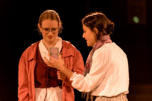 Zwei Frauen in historischer Kleidung auf Bühne, eine hält Karte, andere schaut zu