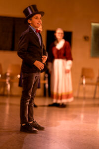 Junge in schwarzem Zylinder und Anzug mit roter Fliege steht vor verschwommener Person im Kleid.