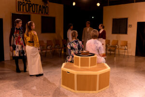 Szenenaufnahme mit sieben Personen auf einer Bühne mit sechseckigem Podest und Schriftzug IPPOPOTAMO.