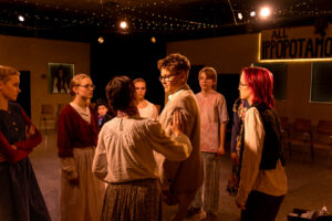 Jugendliche in Theaterkostümen proben auf einer Bühne mit Schild "ALL' IPPOPOTAMO".